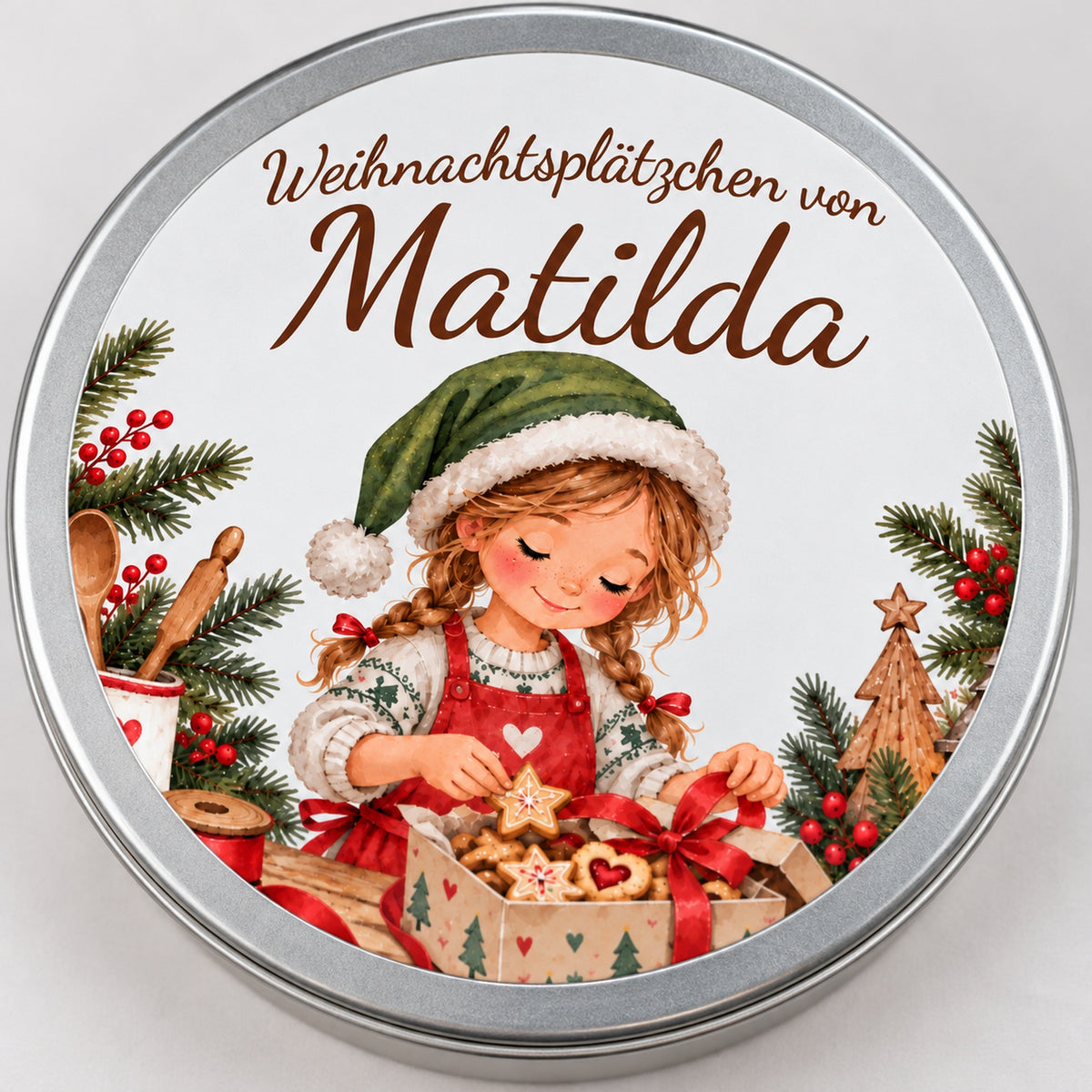 Nahaufnahme des Namens und des Aquarellmotivs einer Weihnachtsbäckerin beim Verpacken eines Keksgeschenks auf dem Dosendeckel.