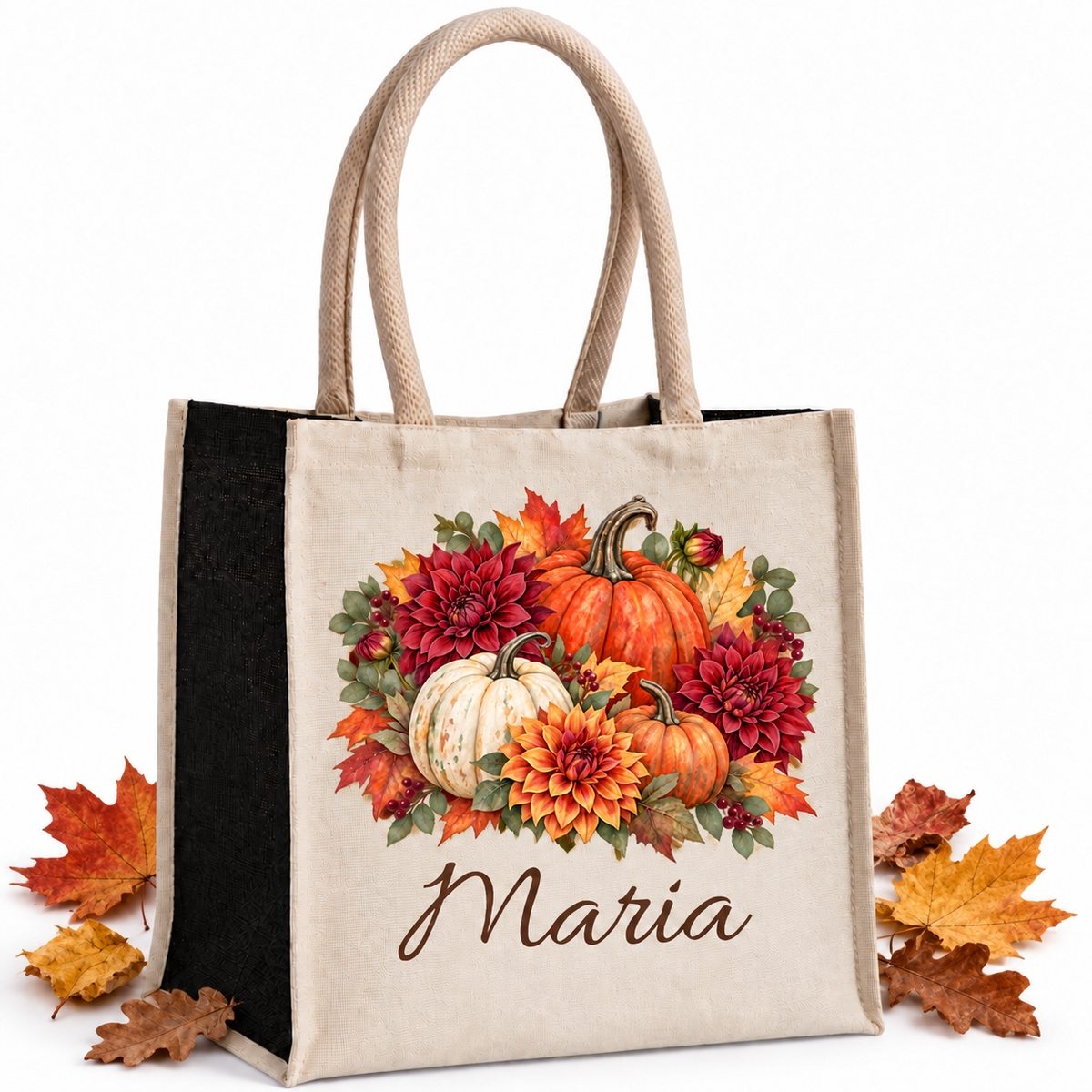 Baumwoll-Jute-Tasche mit Kürbis und Dahlien und Wunschname, naturfarbene Front und schwarze Seiten, mit echten Herbstblättern neben der Tasche auf hellem Hintergrund.