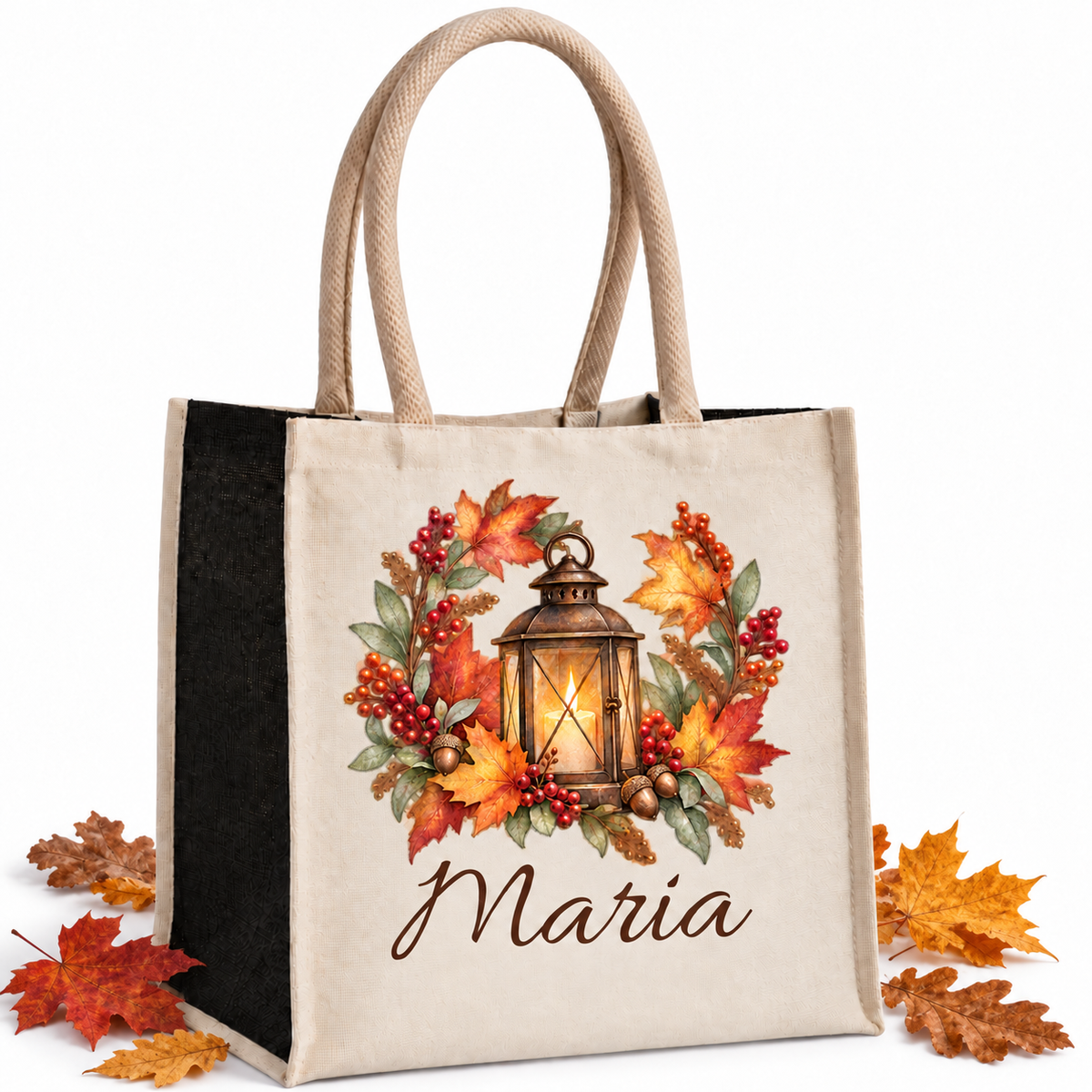 Baumwoll-Jute-Tasche mit Laterne im Herbstkranz und Wunschname, naturfarbene Front und schwarze Seiten, mit echten Herbstblättern neben der Tasche auf hellem Hintergrund.