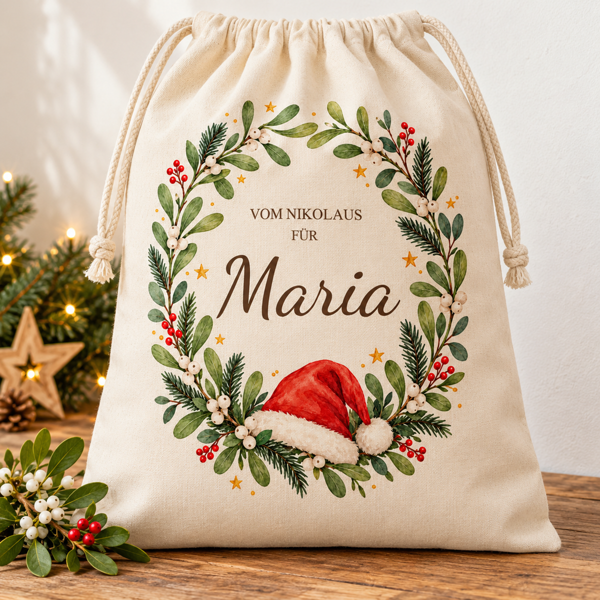 Naturfarbener Nikolaussack mit roter Mütze im grünen Mistelkranz und Wunschname in weihnachtlicher Umgebung.