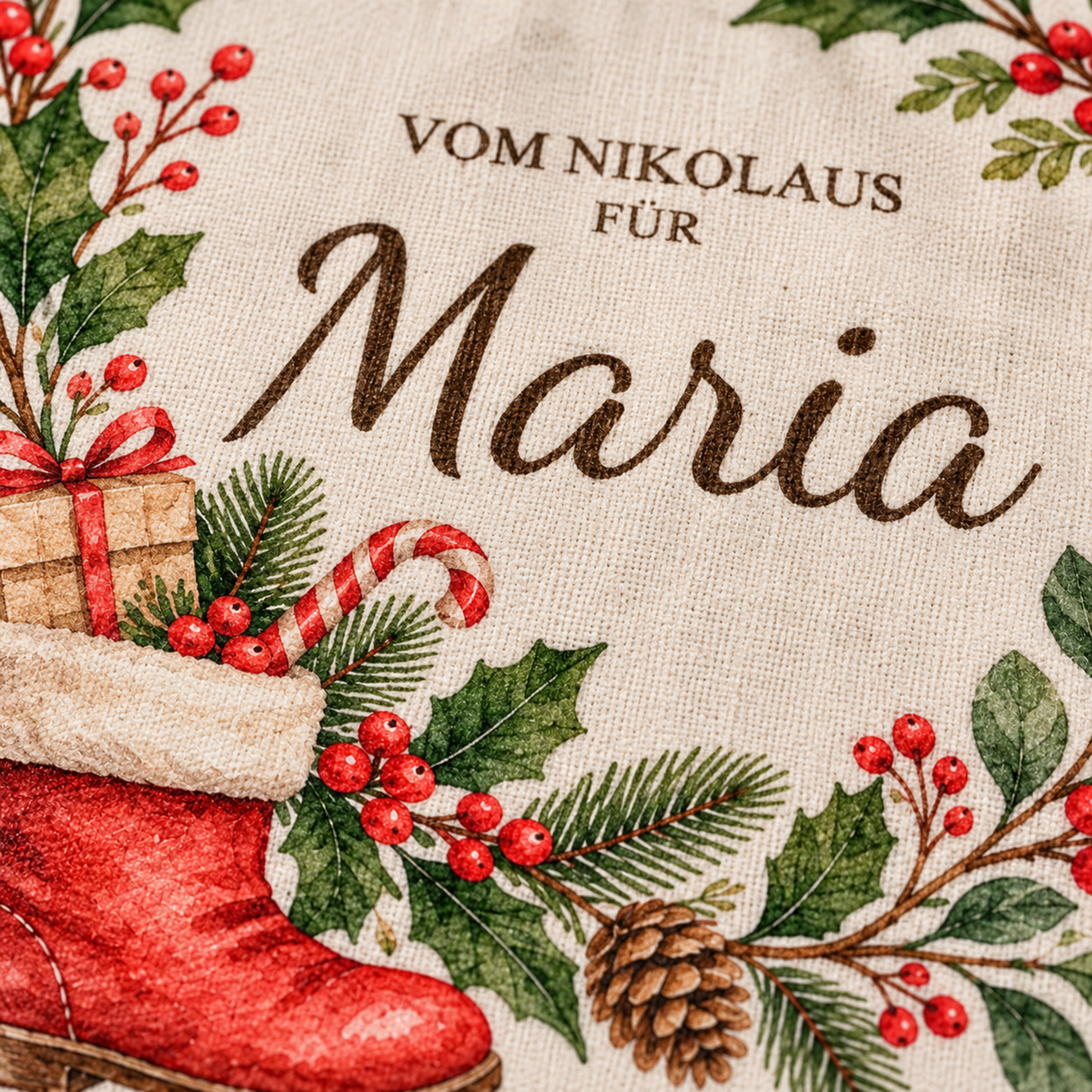 Nahaufnahme der Baumwollstruktur, des Wunschnamens und des gefüllten roten Nikolausstiefels zwischen grünen Blättern und roten Beeren.