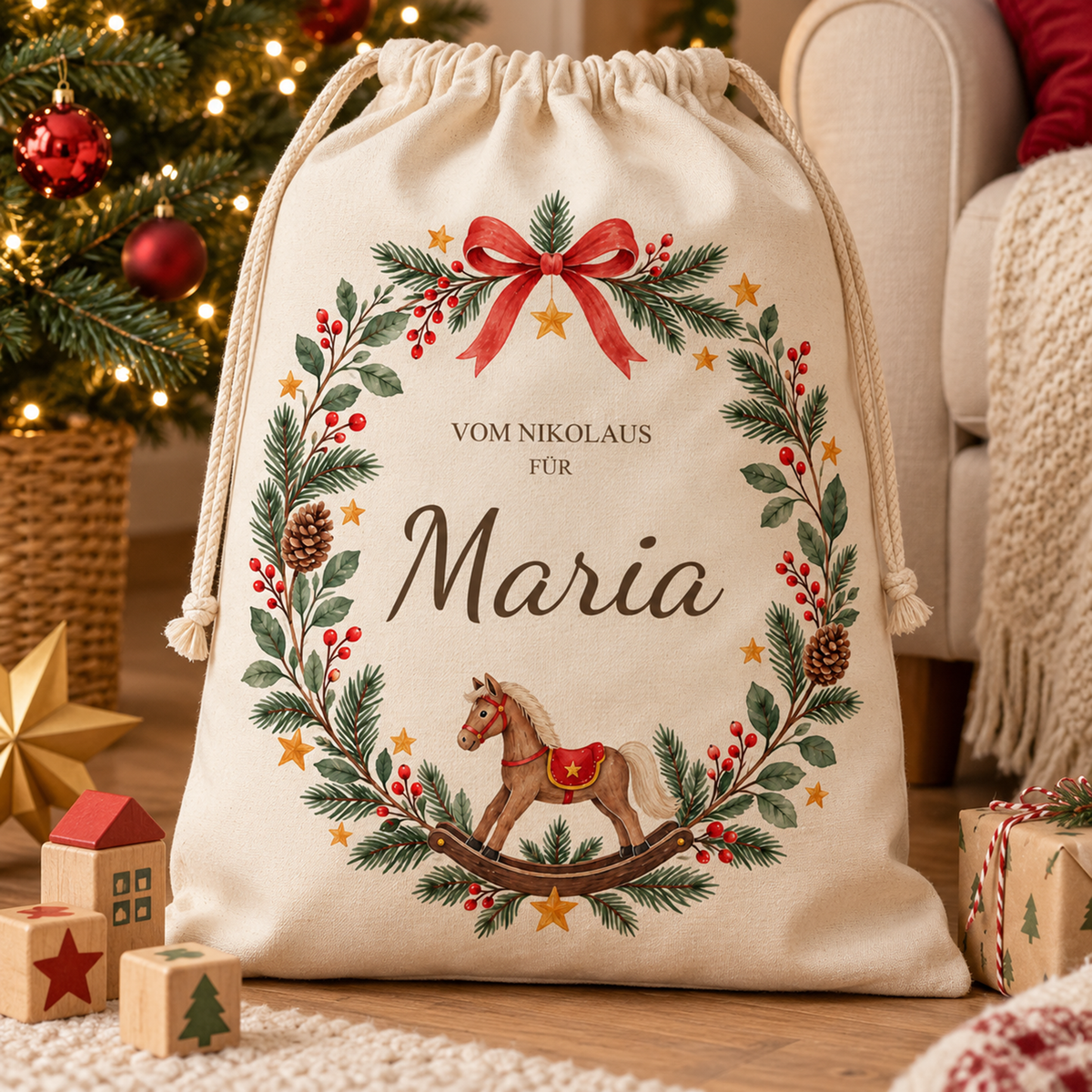 Nikolaussack mit Schaukelpferdkranz und Wunschname vor einem hellen Sessel neben dem Weihnachtsbaum; davor liegen Holzklötze, daneben ein Geschenk.