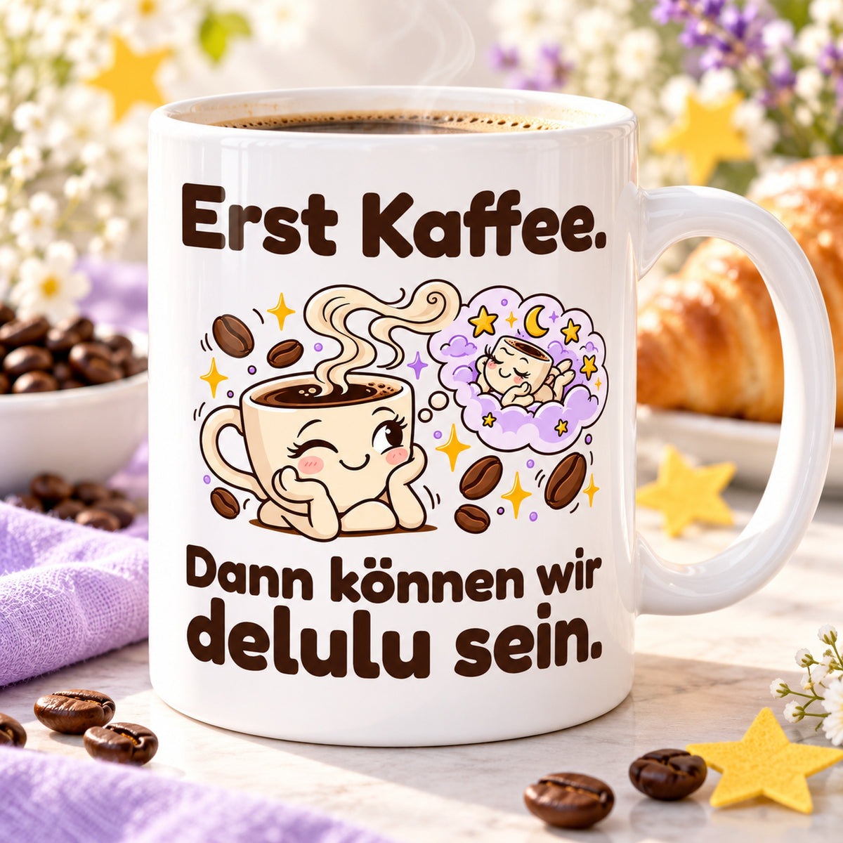 Weiße Keramiktasse mit dem Spruch „Erst Kaffee. Dann können wir delulu sein.“ und farbigem Cartoonmotiv auf hellem Tisch mit lila Tuch und Sternen.
