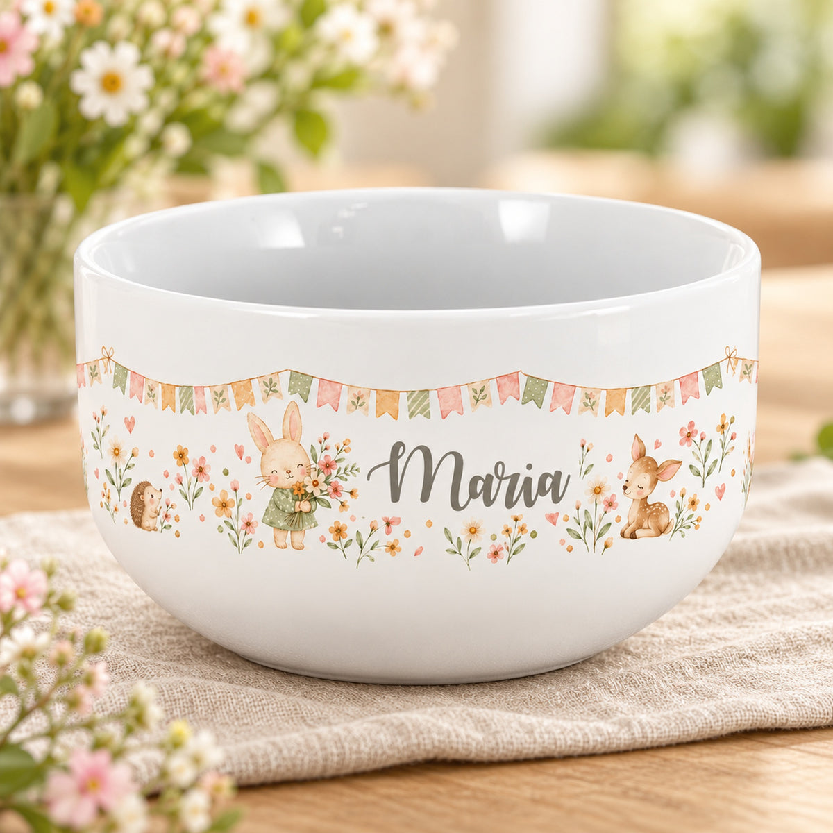 Personalisierte Keramik-Müslischale mit Häschen mit Blumenstrauß, Igel und Rehkitz und Blumen auf einem hellen Tisch.