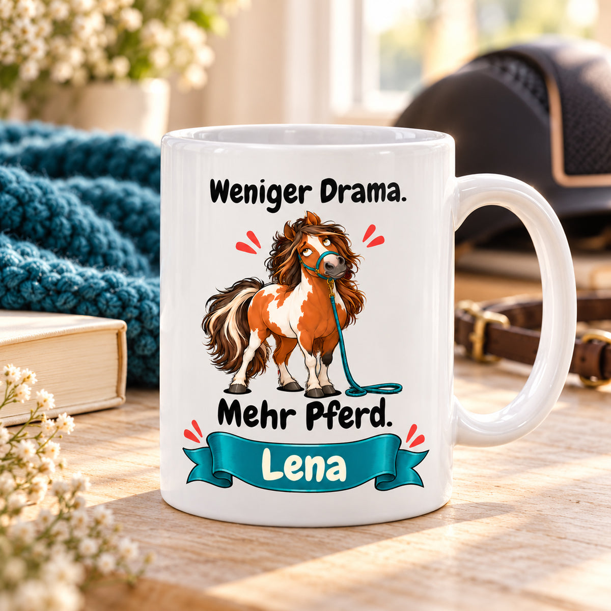 Weiße Pferdetasse mit Namen, Schecken mit petrolfarbenem Strick und Spruch „Weniger Drama. Mehr Pferd.“, in einer gemütlichen Reitstall-Umgebung.