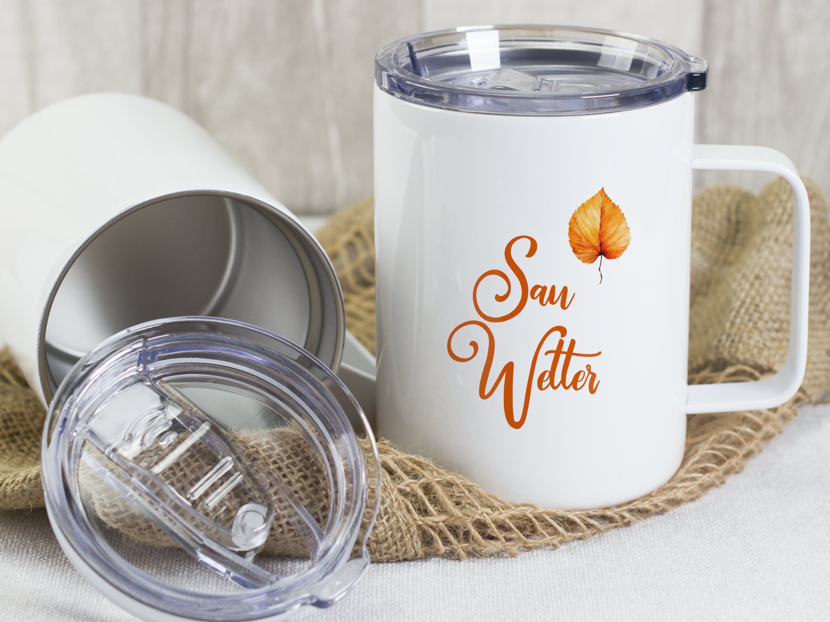Weißer Becher mit "Sau Wetter"-Aufdruck und orangefarbenem Blatt.