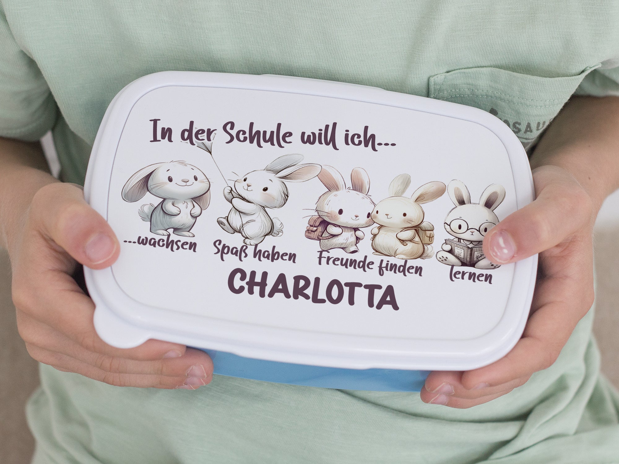 Bento-Box in Weiß mit bunten Hasen und Text.