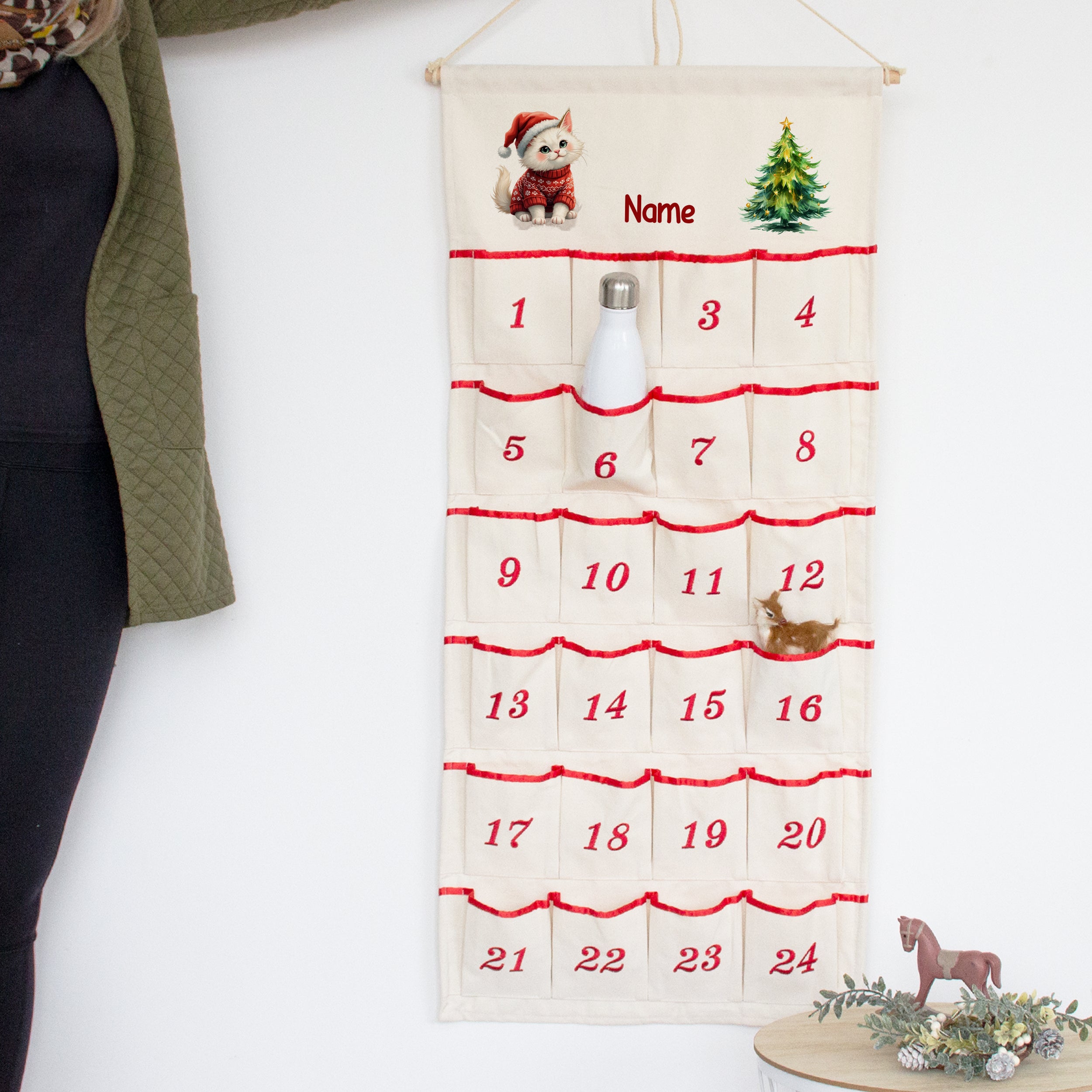 Adventskalender mit Wunschname und Kätzchen, an der Wand mit Flasche in einer nummerierten Tasche