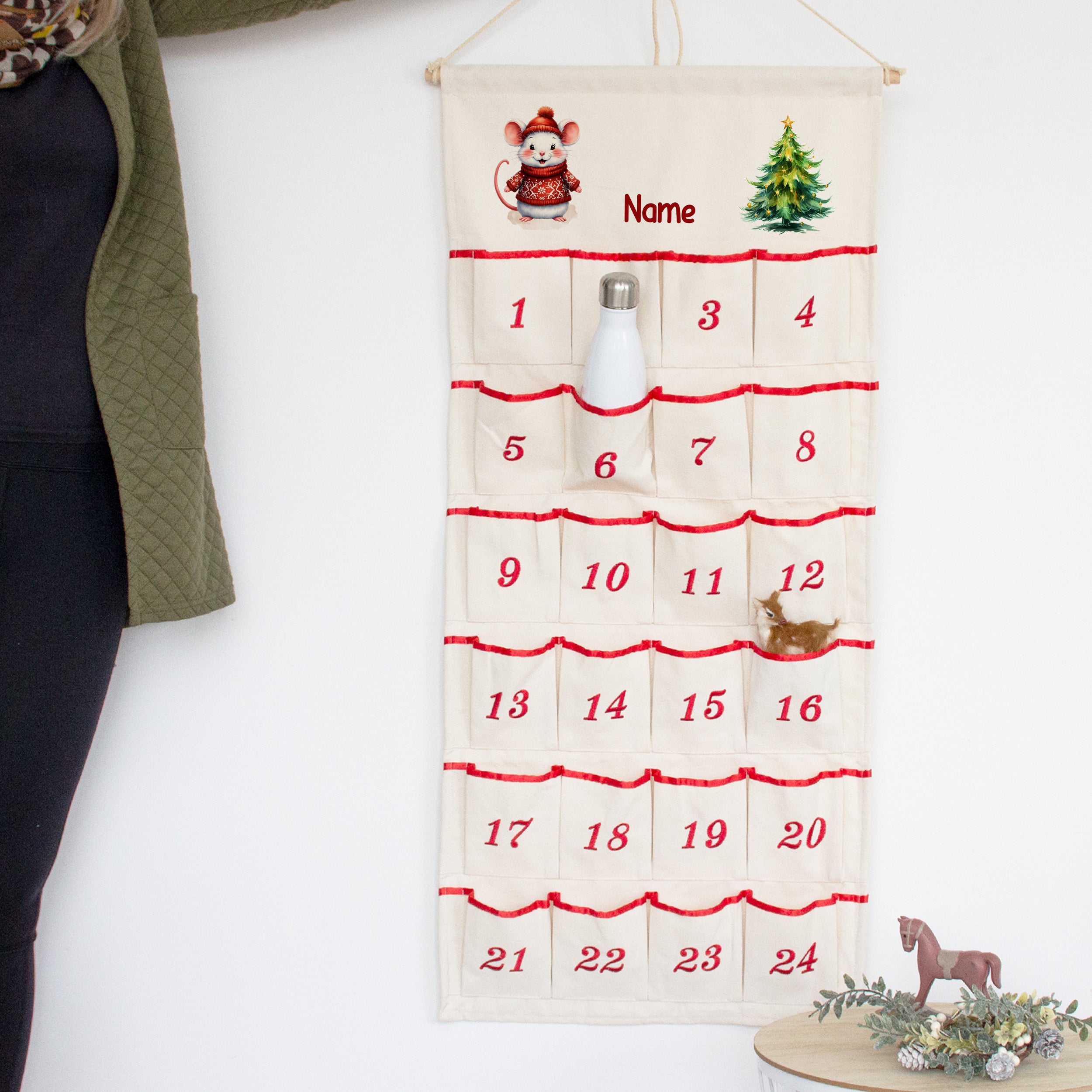 Adventskalender mit Wunschname und Maus, an der Wand mit Flasche in einer nummerierten Tasche
