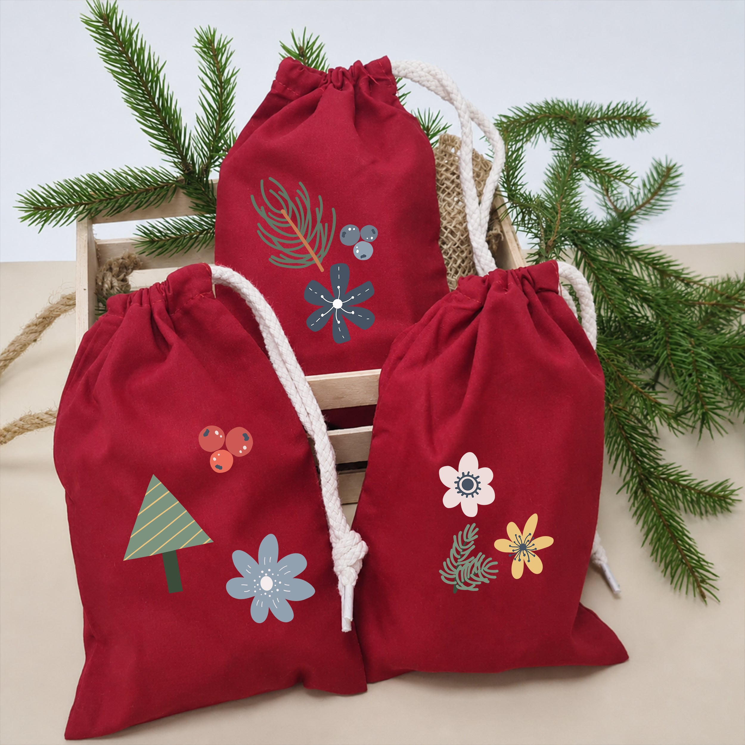 Rote Stoffsäckchen mit aufgebügelten Winterblumen, Beeren, Zweigen und Tannenbaum