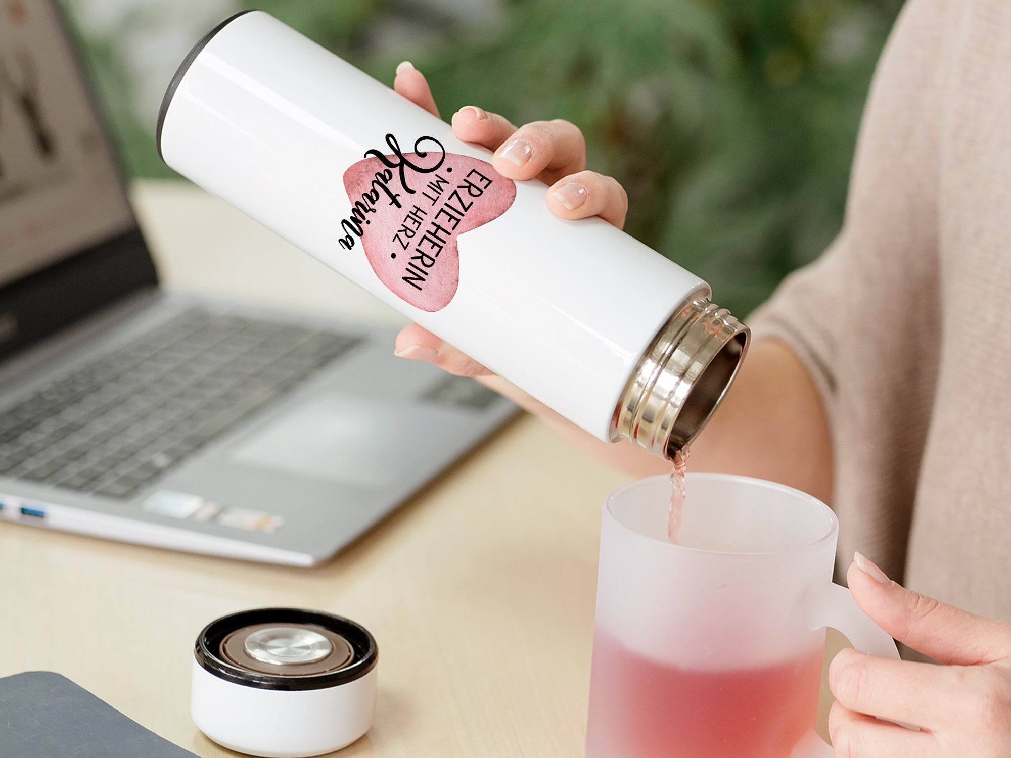 Weißer Thermobecher mit pinkem Aufdruck, Tee wird eingeschenkt.