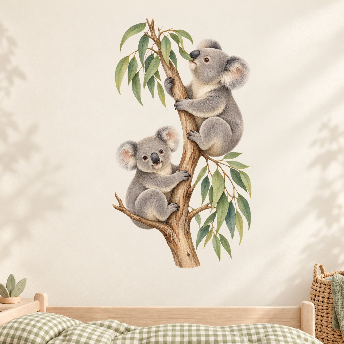 Koala-Wandtattoo Blätterglück an einer cremefarbenen Kinderzimmerwand über einem Holzbett mit grün kariertem Stoff.