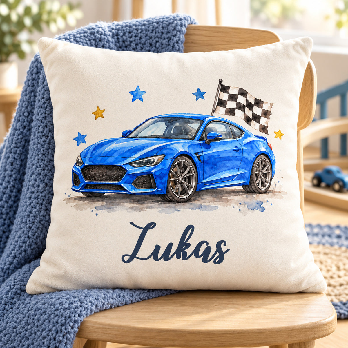 Sportwagen-Kissen mit Namen Lukas auf einem Sessel neben einer blauen Strickdecke.