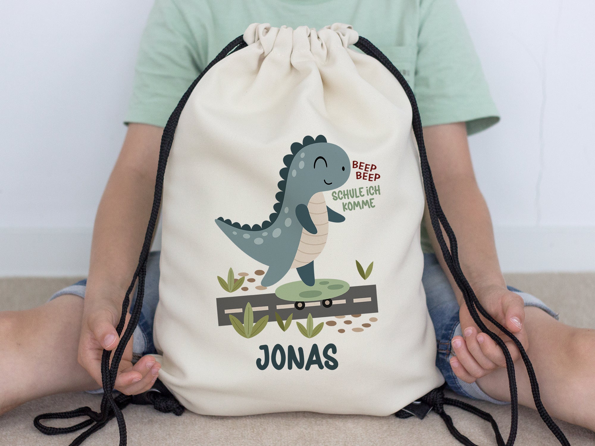 Beiger Rucksack mit Dinosaurier-Motiv und Name Jonas.