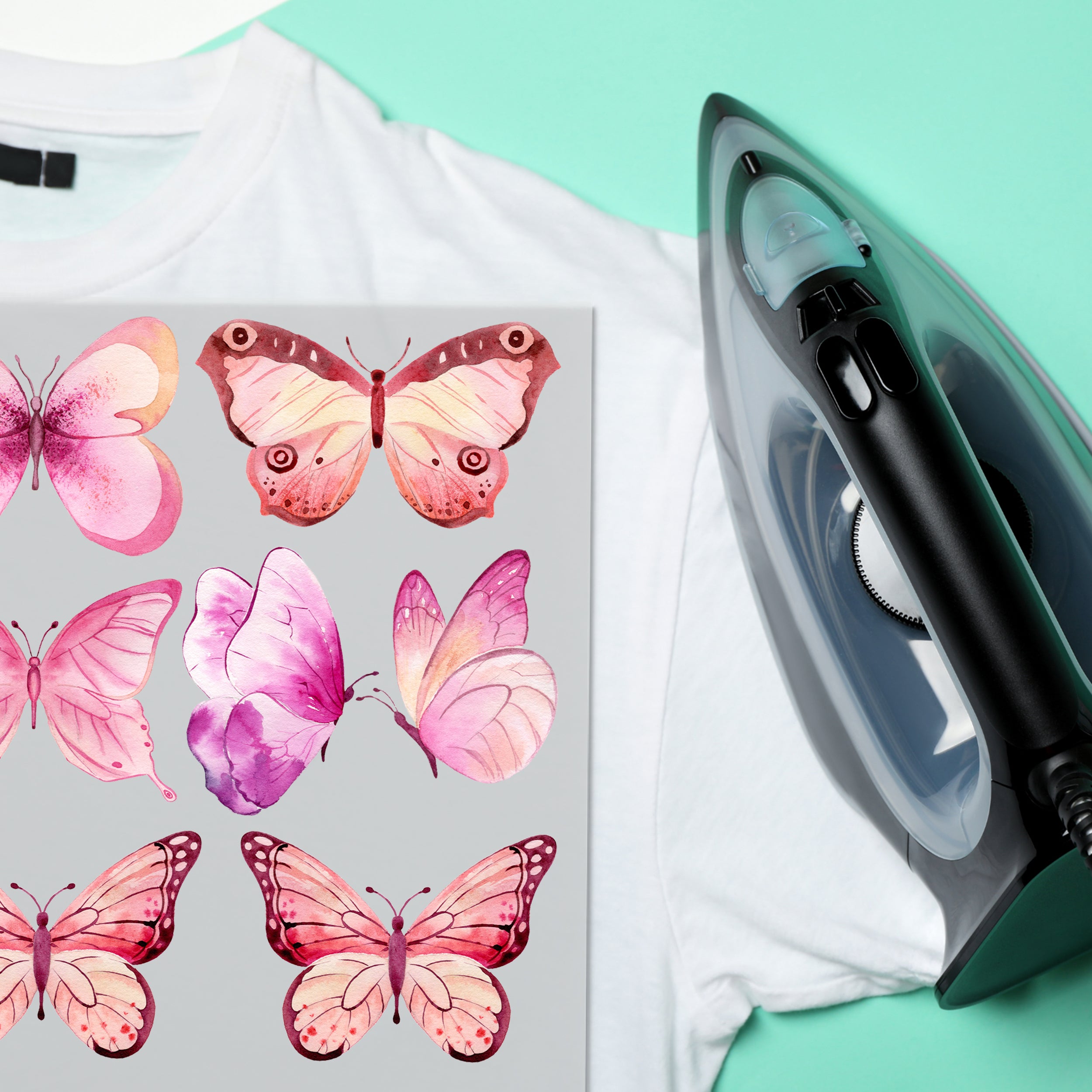 Weißes T-Shirt mit rosa Schmetterlingsmotiven und Dampfbügeleisen.