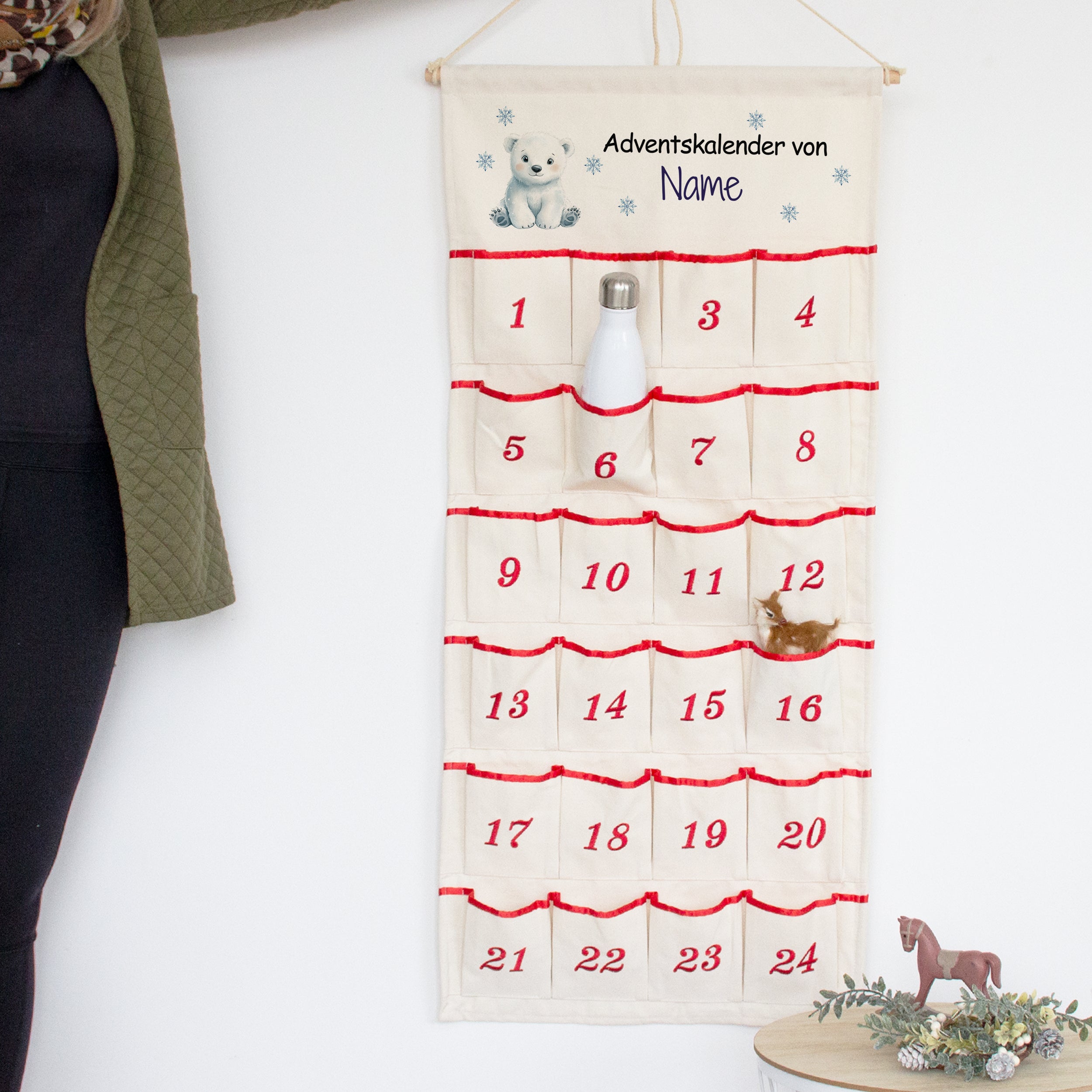Adventskalender mit Wunschname und Eisbär, an der Wand mit Flasche in einer nummerierten Tasche