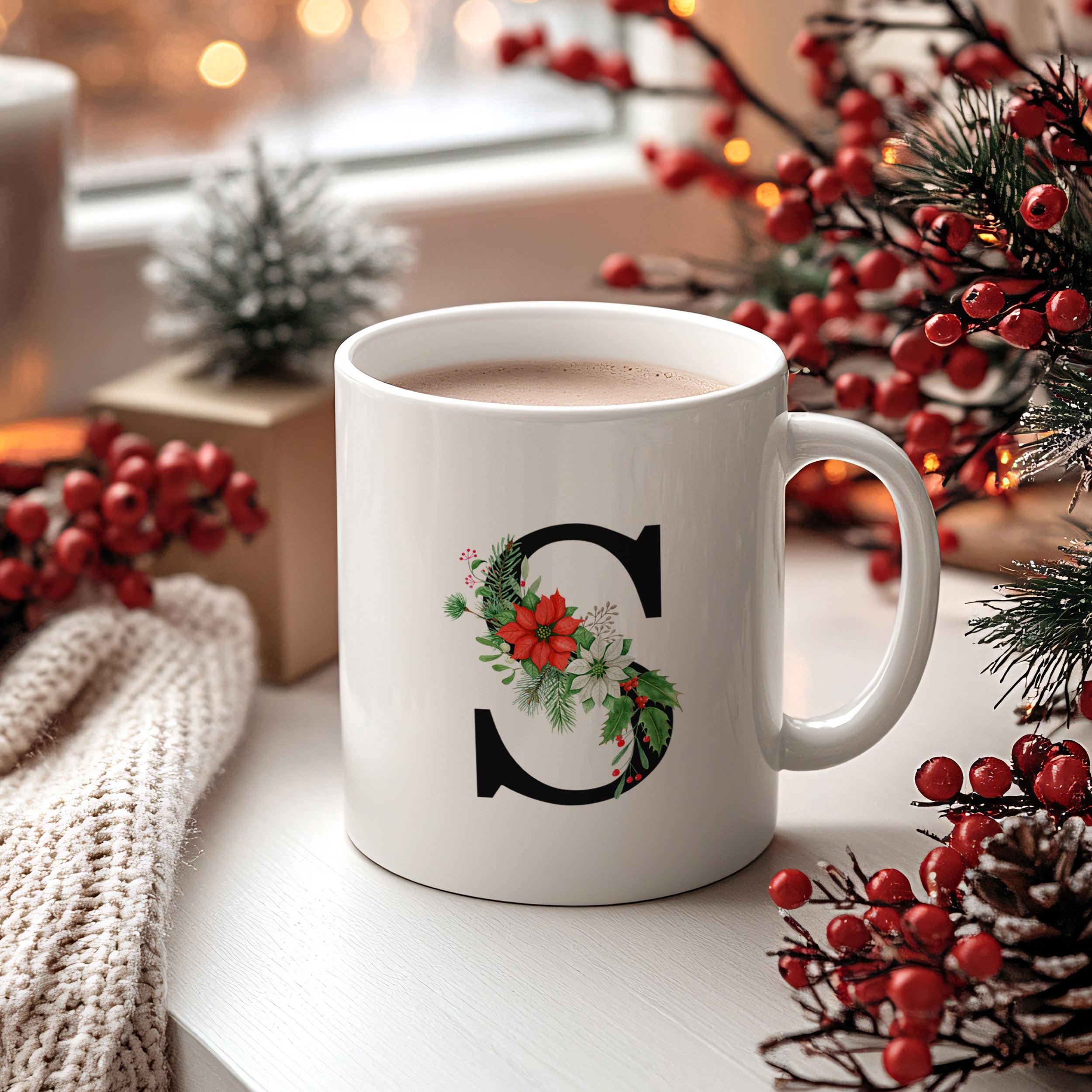 Weiße Tasse mit schwarzem "S" und weihnachtlichem Dekor.
