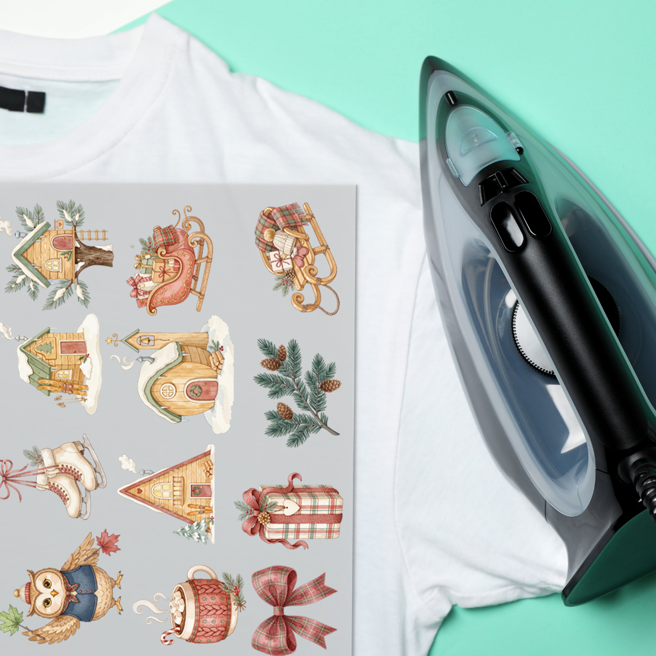 Winterliche Bügelbilder mit Holzhäusern, Schlitten und Geschenk auf weißem T-Shirt neben einem Bügeleisen