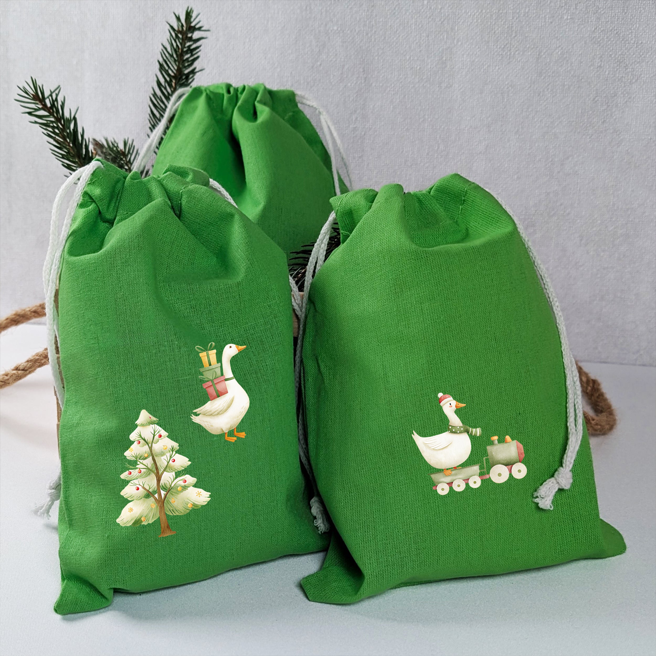 Grüne Stoffsäckchen mit aufgebügelten Weihnachtsgänsen, Tannenbaum, Geschenken und Eisenbahn