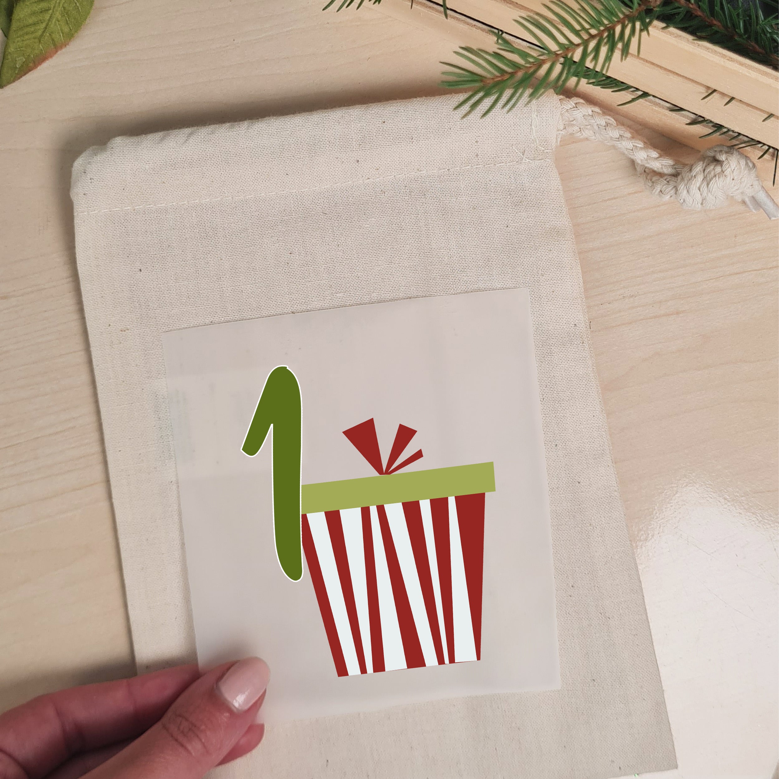 Bügelbild mit Geschenk und Zahl 1 wird auf einen naturfarbenen Stoffbeutel aufgelegt