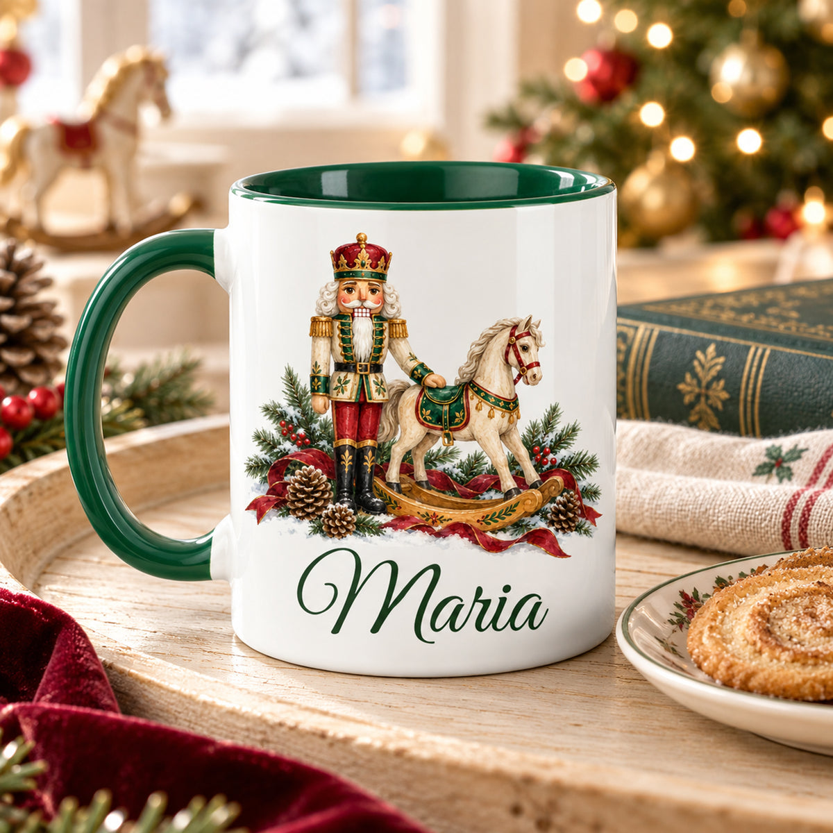 Weiße Keramiktasse mit grünem Henkel und grüner Innenseite, Motiv Nussknacker mit Schaukelpferd und Wunschname auf einem Tablett mit Gebäck in weihnachtlicher Umgebung.