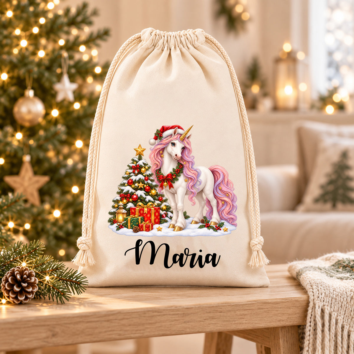 Nikolaussack mit weißem Einhorn mit rosa-lilafarbener Mähne neben Weihnachtsbaum und Geschenken und dem Namen Maria auf einer hellen Holzablage in weihnachtlicher Wohnumgebung.