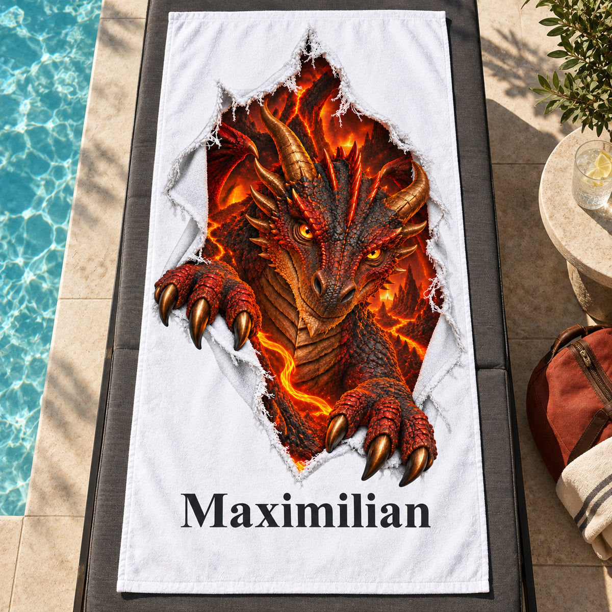 Weißes personalisiertes Handtuch mit Feuerdrache-Motiv im Stoffriss-Design auf einer dunklen Liege am Pool neben einer rotbraunen Tasche.